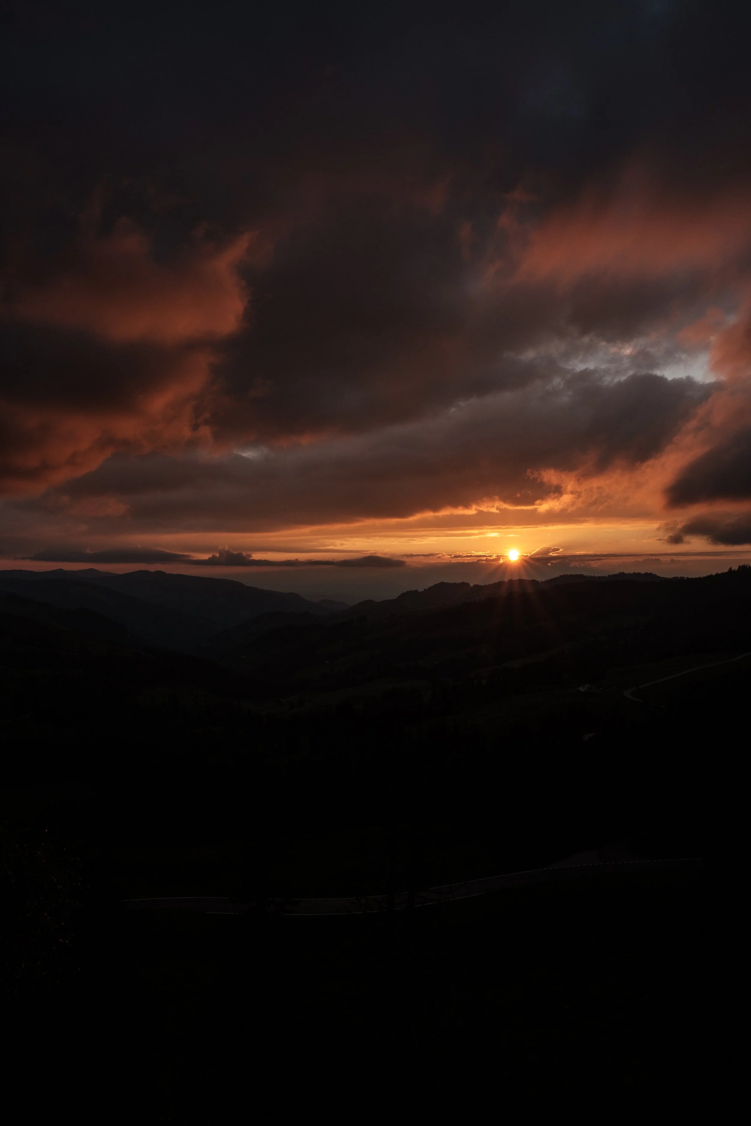 Ein Sonnenuntergang hinter Hügeln mit dunklen Wolken am Himmel.