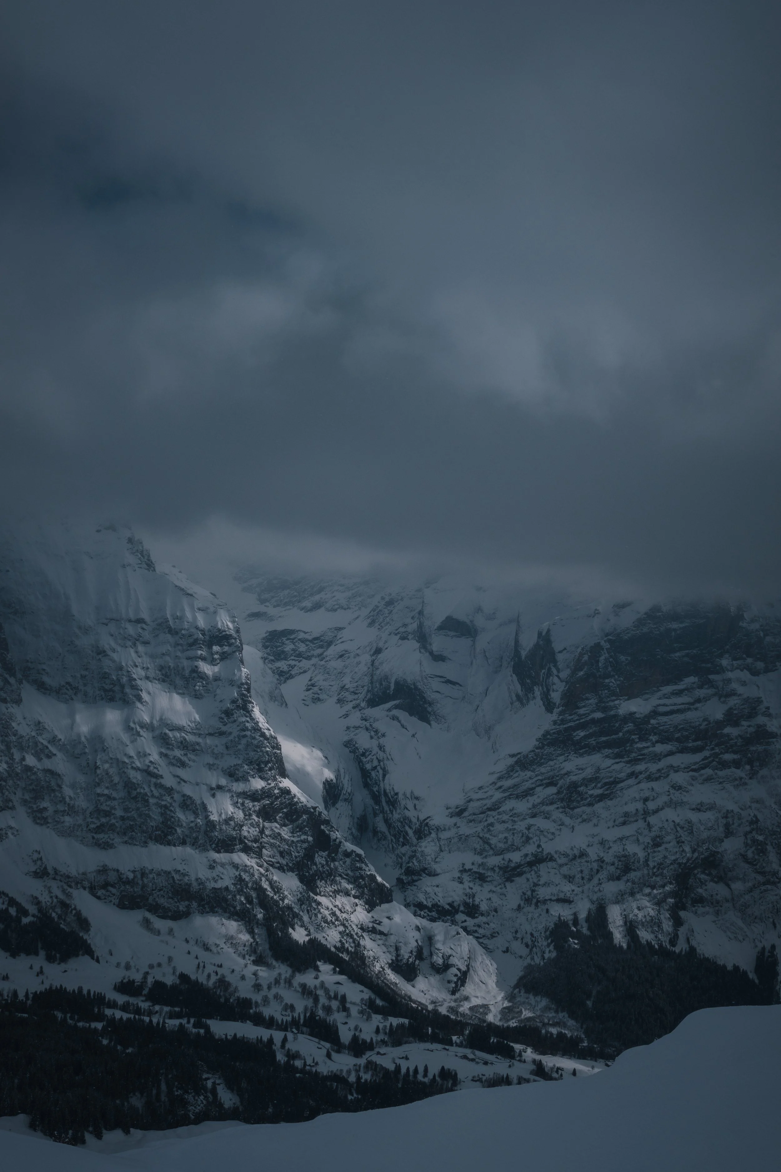 Schneebedeckte Berge und dunkle Wolken am Himmel in einer verschneiten Landschaft.
