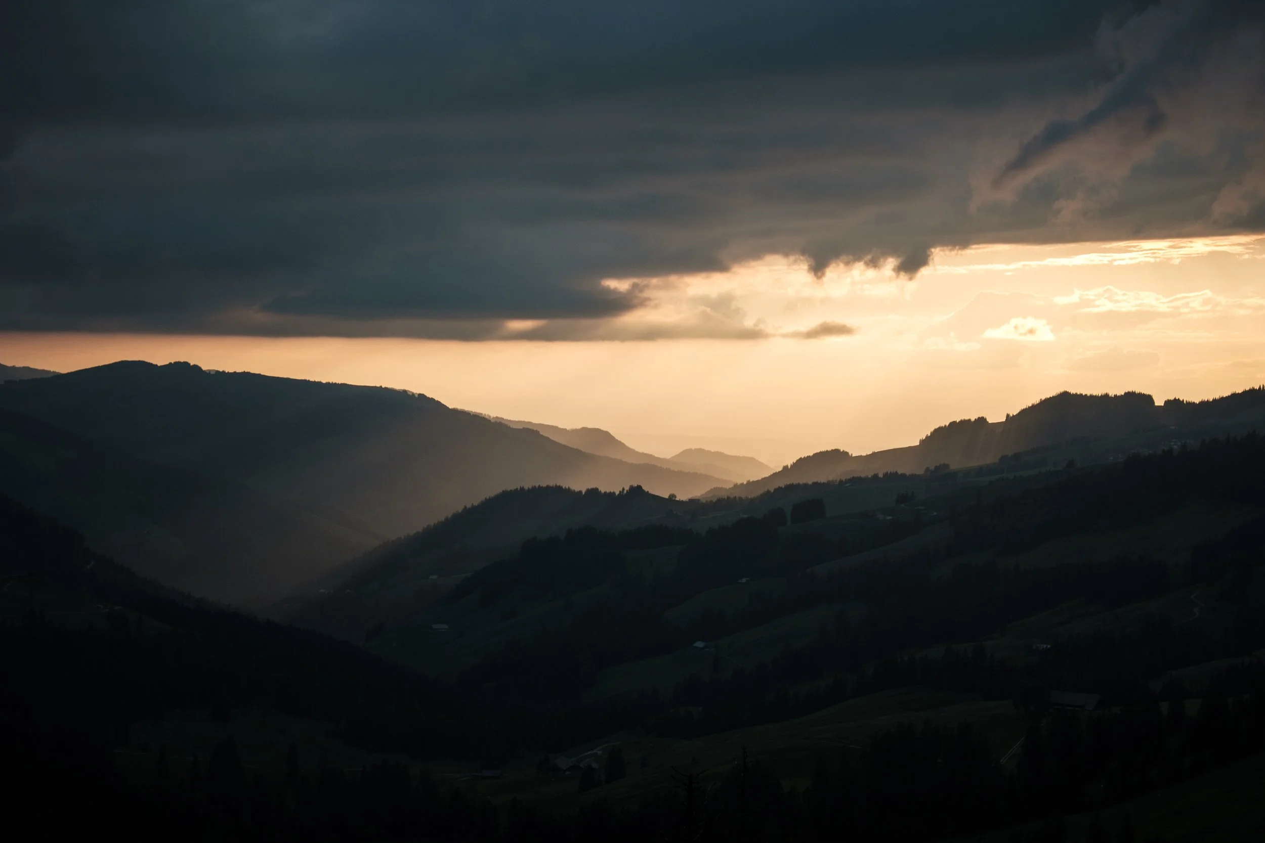 Berglandschaft bei Sonnenuntergang mit dunklen Wolken am Himmel.