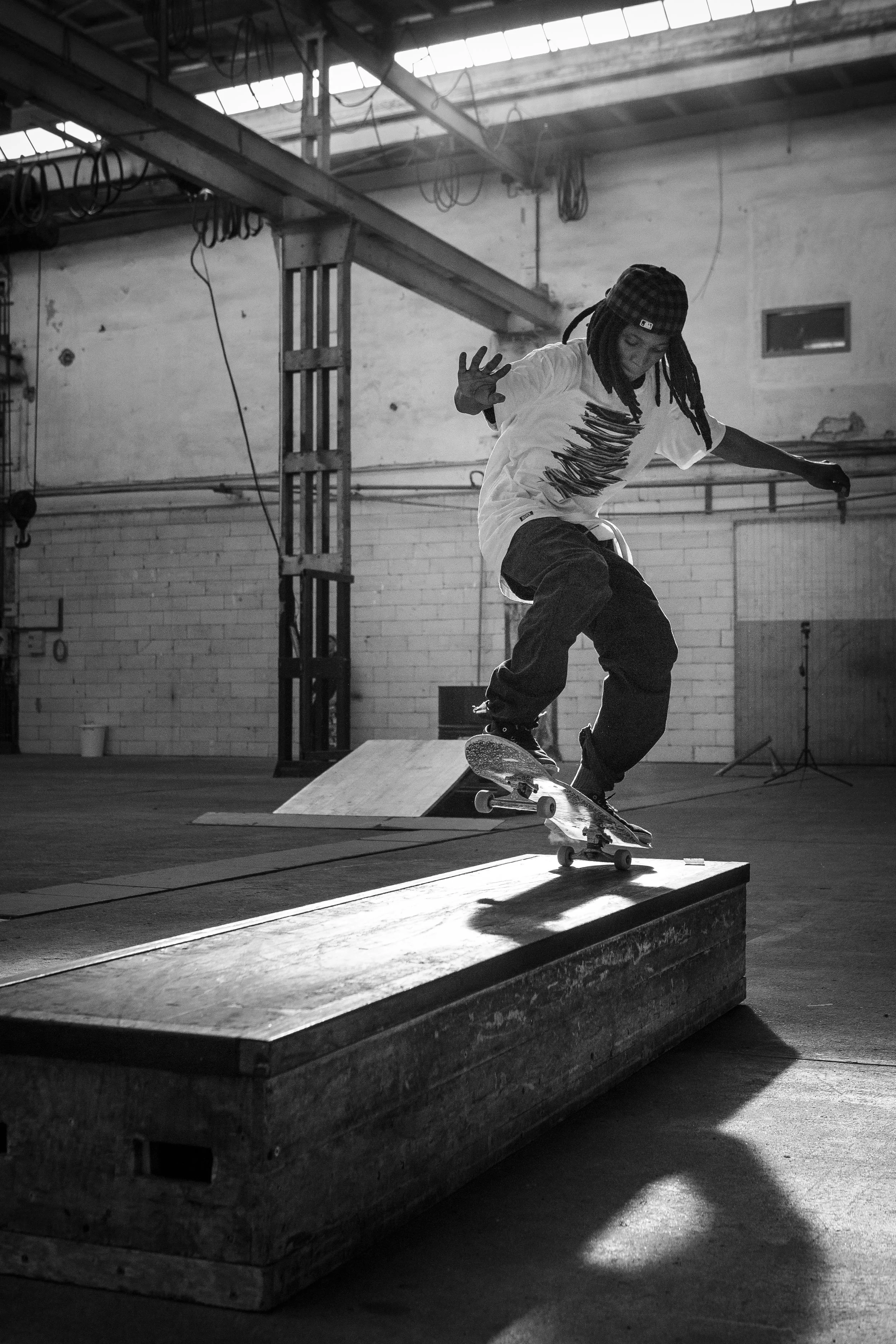 Skater beim Trick auf einer Holz-Balken in einer Indoor-Skatehalle, schwarz-weiß Fotografie.