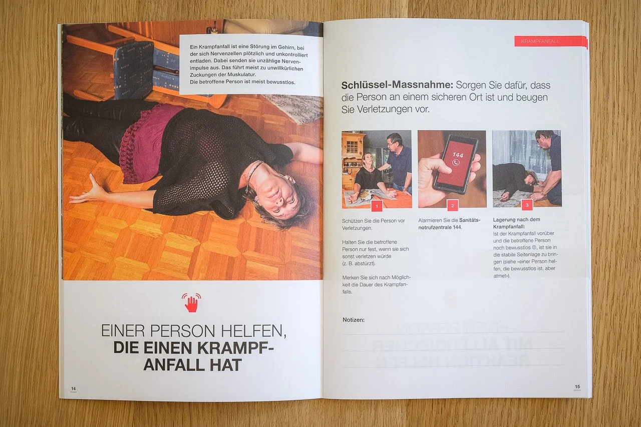Offene Broschüre mit einem Bild einer Person, die bewusstlos am Boden liegt, und Anweisungen zur Erkennung und Erste Hilfe bei einem Krampfanfall. Text erklärt Maßnahmen zur Unfallverhütung und Erste Hilfe bei Krampfanfällen.