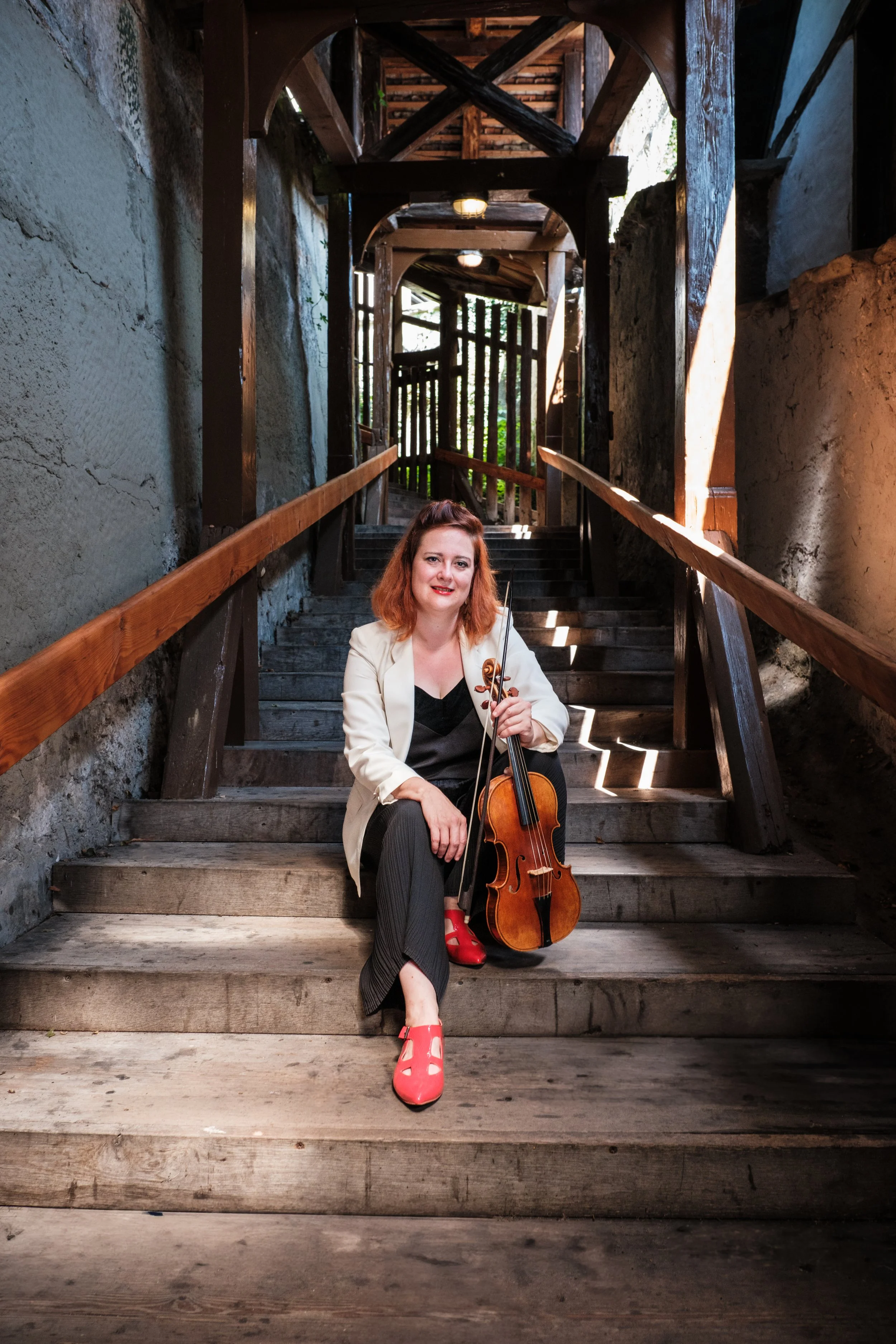 Frau mit Cello auf Holzstufen in einer alten, halb unterirdischen Struktur.