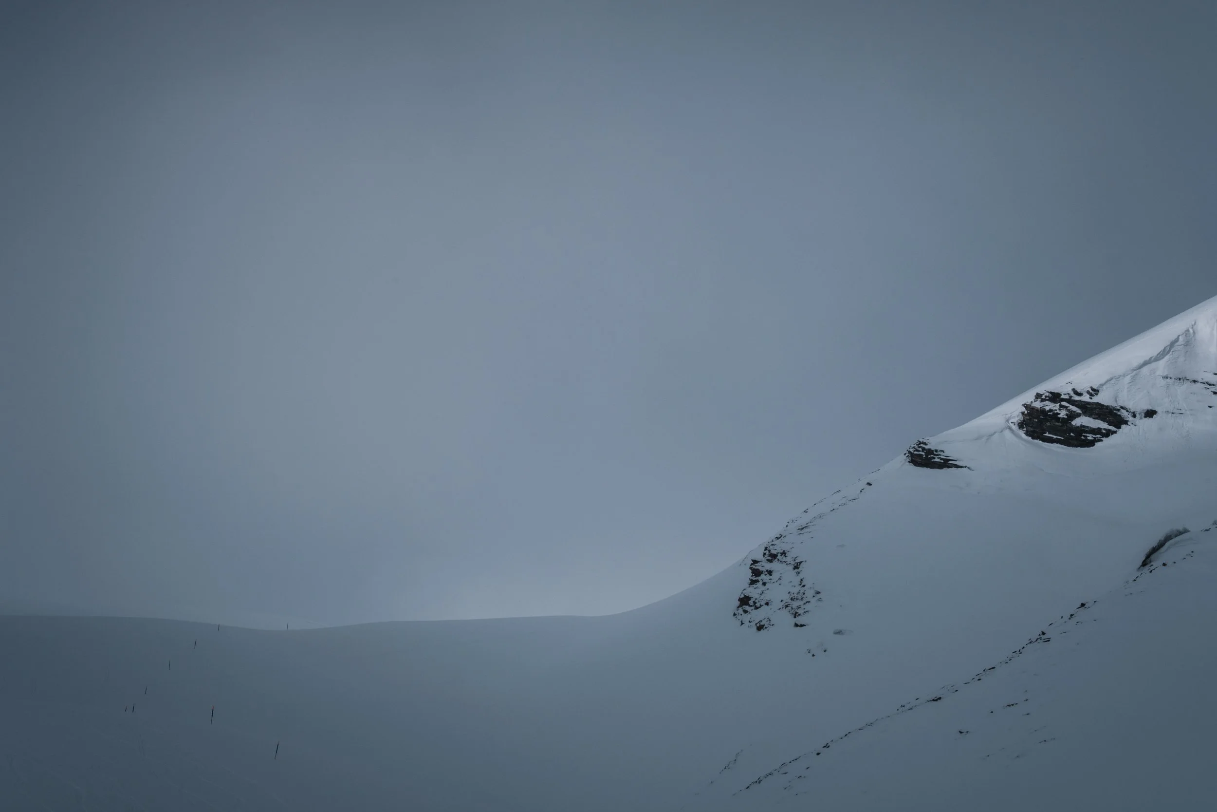 Schneebedeckter Berg mit dunklen Felsklippen unter grauem Himmel.