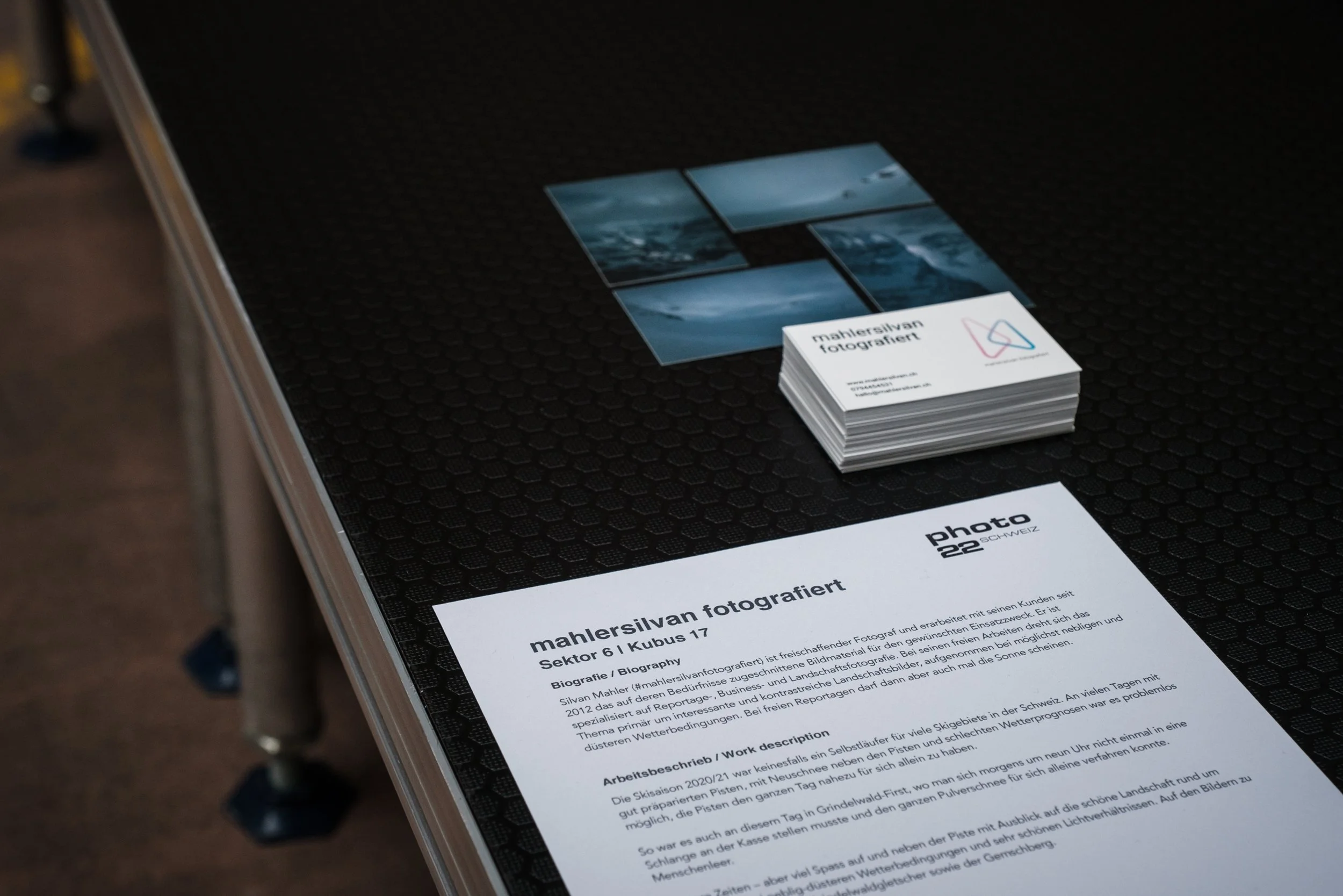 Decken mit Fotoprints, Visitenkarte und einem Blatt mit Text auf einem schwarzen Oberflächenmuster.