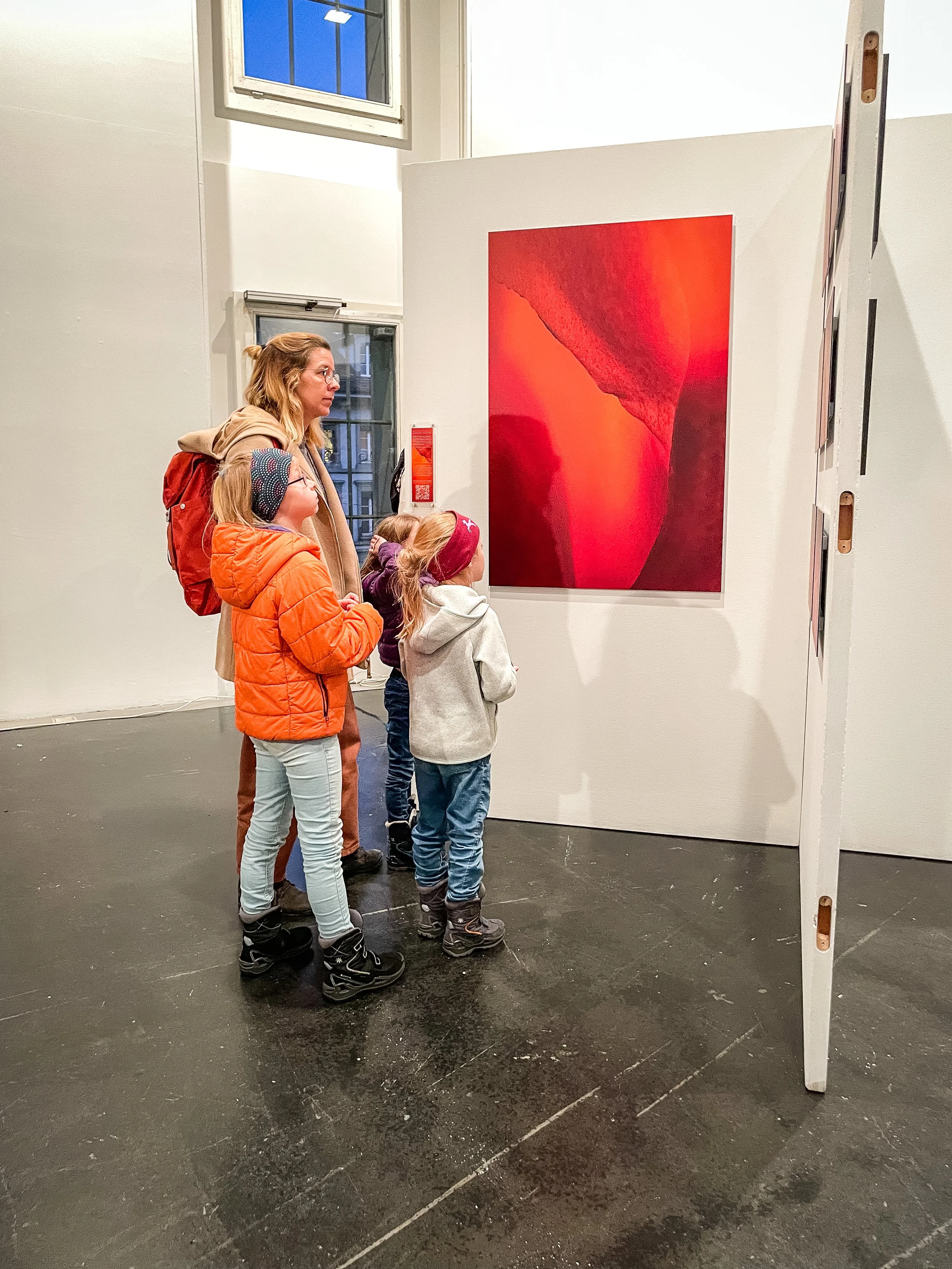 Eine Gruppe von Kindern und einer Erwachsenen betrachten ein rotes abstraktes Gemälde in einer Kunstgalerie.